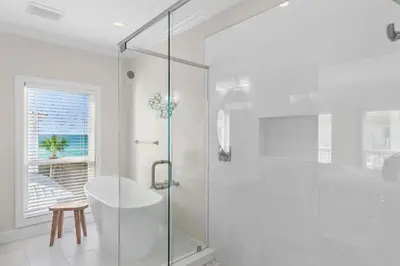 a white bathroom with a glass shower stall and a stool at Fintastic in Santa Rosa Beach