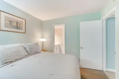 a white bedroom with a bed and a lamp at Gulf-View Balcony Beachfront Condo in PCB! in Panama City Beach