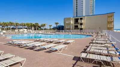 a swimming pool with chaise lounges and chairs next to a building at Tidewater Escape: 1BR/2BA beachfront condo, sleeps 6, Gulf views & comfort! in Panama City Beach
