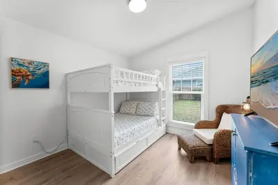 a white bedroom with a bunk bed and a chair at Aqua Believe It in Panama City Beach