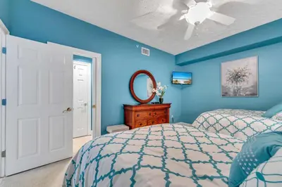 a blue bedroom with a bed and a ceiling fan at Hidden Dunes 503 in Panama City Beach