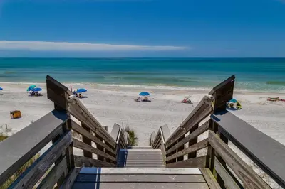 a staircase leading to a beach with umbrellas at Hidden Beach Villas 122 - A Sunset Paradise in Santa Rosa Beach