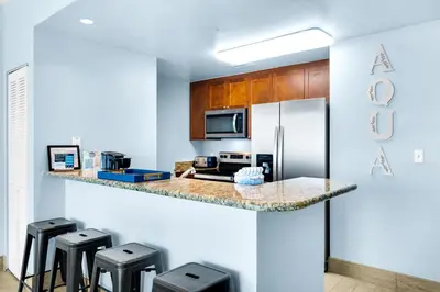 a kitchen with a counter with stools and a refrigerator at Aqua 1904 in Panama City Beach