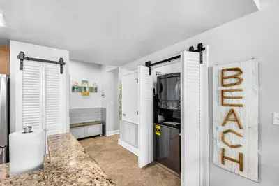 a kitchen with white walls and a door with a tv at Aqua 1609 in Panama City Beach