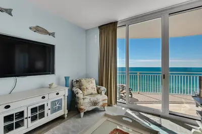 a living room with a television and a balcony at Aqua 1402 in Panama City Beach