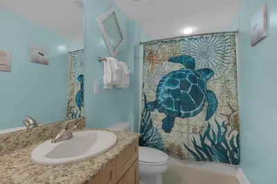 a bathroom with a turtle tile on the shower curtain at Aqua 1711 in Panama City Beach