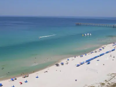 a beach with people and umbrellas and a pier at Aqua 0502 in Panama City Beach