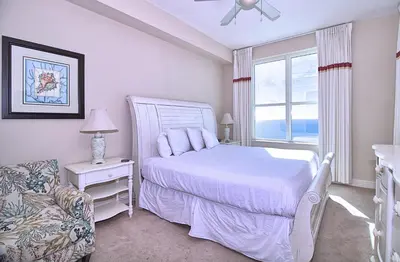 a bedroom with a bed and a chair and a window at Aqua 2206 in Panama City Beach