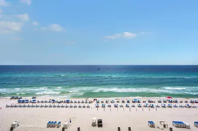 a beach with chairs and umbrellas and the ocean at Aqua 0610 in Panama City Beach