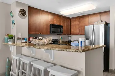 a kitchen with a counter with stools and a refrigerator at Aqua 1106 in Panama City Beach