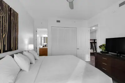 a white bedroom with a large bed and a flat screen tv at Aqua 2211 in Panama City Beach