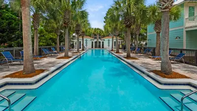 a swimming pool with palm trees and chairs at The Cake Cottage in Santa Rosa Beach