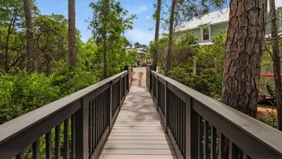 a wooden bridge leading to a house with trees at The Cake Cottage in Santa Rosa Beach