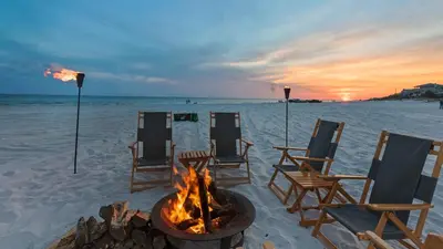 a fire pit on a beach with chairs and the ocean at The Cake Cottage in Santa Rosa Beach
