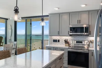 a kitchen with white cabinets and a view of the ocean at Edgewater Windward 508 - Newly Renovated Corner Condominium! in Panama City Beach