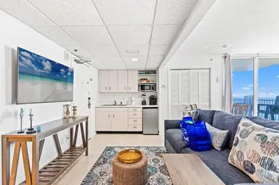 a living room with a blue couch and a kitchen at Coastal Hideaway: Cozy Beachfront Studio – Sleeps 4 with Stunning Views! in Panama City Beach