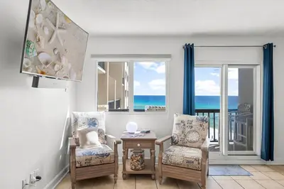 a living room with two chairs and a table and windows at Serenity Found at A-521 in Panama City Beach