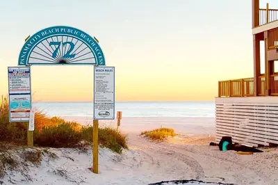 a sign on a beach with a building and the ocean at Paradise found steps to beach in Panama City Beach