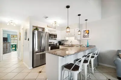 a kitchen with white cabinets and a island with bar stools at Paradise found steps to beach in Panama City Beach