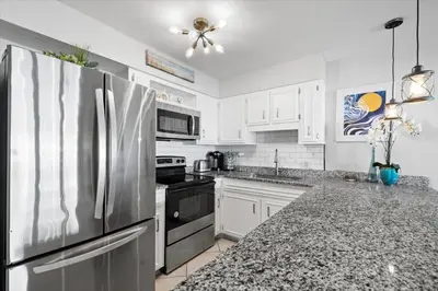 a kitchen with white cabinets and a stainless steel refrigerator at Paradise found steps to beach in Panama City Beach