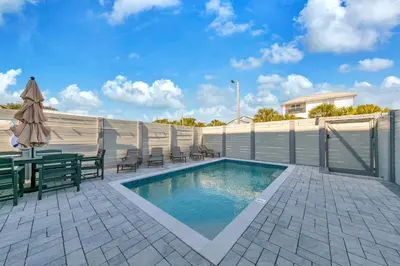 a swimming pool with chairs and an umbrella on a patio at Golden Seashell West in Panama City Beach