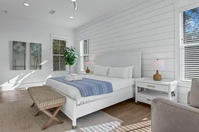 a white bedroom with a bed and a chair at Serenity at Treetop in Inlet Beach