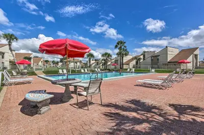 a patio with a table with a red umbrella next to a pool at Walk to Pool and Beach PCB Resort Getaway with Porch in Panama City Beach