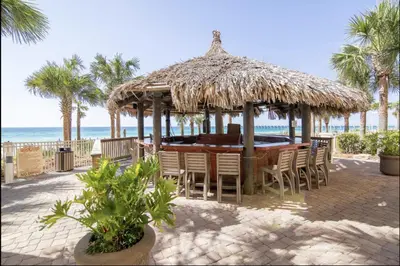 a table and chairs under a straw umbrella on the beach at Calypso Resort By Sand Seeker Vacations in Panama City Beach