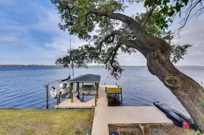 a dock with a tree and a boat on the water at Boat Dock and Game Room Waterfront Panama City Gem in Lynn Haven