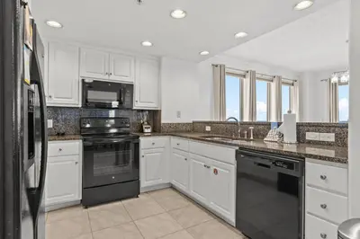 a kitchen with white cabinets and black appliances at Treasure Tides–3BR Beachfront Corner Unit sleeps 8 with Stunning Gulf Views! in Panama City Beach