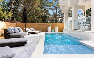 a patio with a swimming pool with chairs and a fence at Sapphire Bay by Oversee 30A in Santa Rosa Beach
