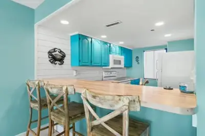 a kitchen with blue cabinets and a counter with chairs at Commodore 202 - Thomas Drive Paradise in Panama City Beach