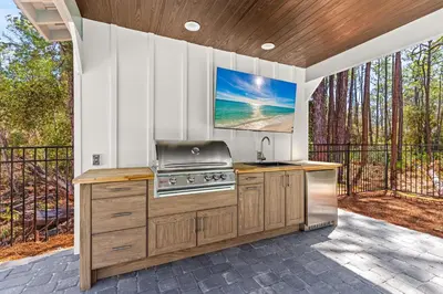 an outdoor kitchen with a grill and a television at Coastal Opulence in Santa Rosa Beach