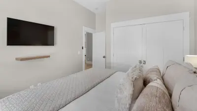 a white bedroom with a couch and a tv on a wall at The Bee's Knees in Santa Rosa Beach