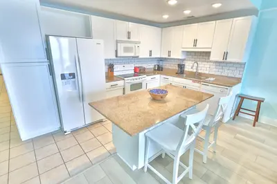 a kitchen with white appliances and a counter with chairs at Lake Town Charming Condo Steps from the Beach in Panama City Beach