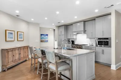 a kitchen with white cabinets and a island with bar chairs at Casa Del Oro Penthouse at Barrett Square - Downtown Rosemary Beach Pool &Hot Tub Access in Rosemary Beach