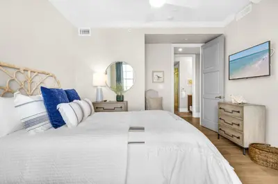 a white bedroom with a large bed with blue pillows at Casa Del Oro Penthouse at Barrett Square - Downtown Rosemary Beach Pool &Hot Tub Access in Rosemary Beach
