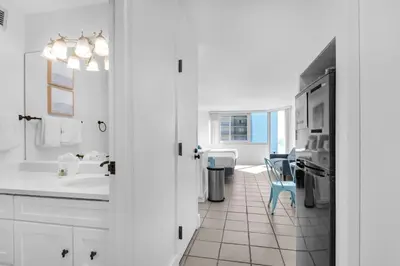 a white bathroom with a sink and a blue chair at Top of the Gulf 507 Beach Front Resort Ocean View in Panama City Beach