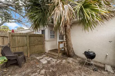 a backyard with a palm tree and a grill and a fence at Cowboy Cottage by Beach Haven Vacation Rentals in Panama City Beach