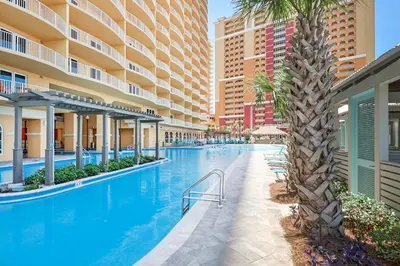 an infinity pool with a palm tree and buildings at Calypso 3-2007 by Emerald Coast Retreats in Panama City Beach