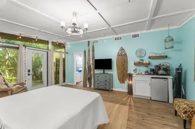 a bedroom with blue walls and a white bed and a kitchen at Zen Studio by Beach Haven Vacation Rentals in Panama City Beach