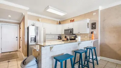 a kitchen with two blue stools at a counter at Emerald Isle 403 by Emerald Coast Retreats in Panama City Beach