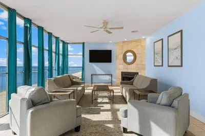 a living room with chairs and a tv and windows at Sharkys Retreat 701 by Beach Haven Vacation Rentals in Panama City Beach