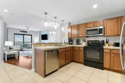 a kitchen with wooden cabinets and appliances and a living room at Origin 1007 - One Bedroom - Sunset View by Beach Haven Vacation Rentals in Panama City Beach
