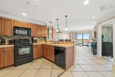 a kitchen with wooden cabinets and black appliances at Origin 0731- One Bedroom - Sunny Gulf Views by Beach Haven Vacation Rentals in Panama City Beach