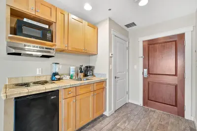 a kitchen with wooden cabinets and a black appliance at Origin 0705 - Studio King Gulf View- Stunning Sunset Views by Beach Haven Vacation Rentals in Panama City Beach