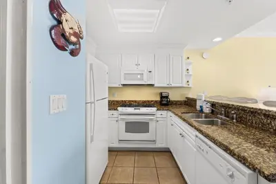 a kitchen with white cabinets and a sink and a refrigerator at Boardwalk Beach Resort #1107 by Book That Condo in Panama City Beach