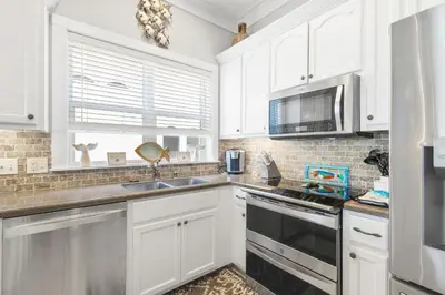 a kitchen with white cabinets and a sink and a microwave at Sandy Shenanigans by Blu Skye! -New to Management 2025! in Panama City Beach