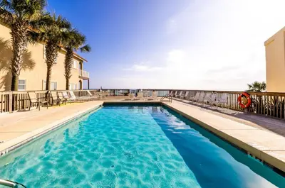 a swimming pool with palm trees and a building at Sandy Shenanigans by Blu Skye! -New to Management 2025! in Panama City Beach
