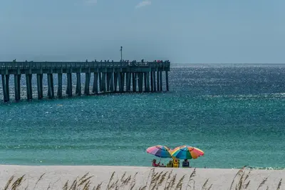 two people under umbrellas on a beach near a pier at Calypso 1-1709 by Emerald Coast Retreats in Panama City Beach